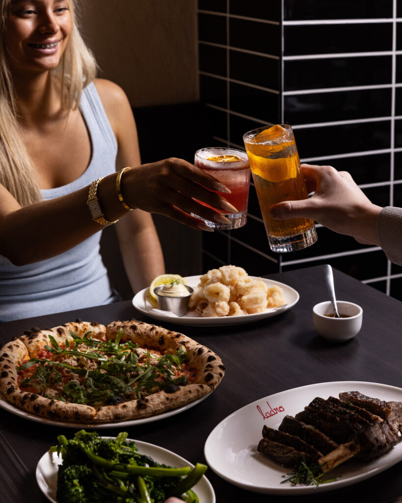 Friends toasting drinks over pizza and appetizers.