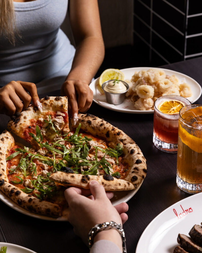 People sharing pizza with drinks and calamari