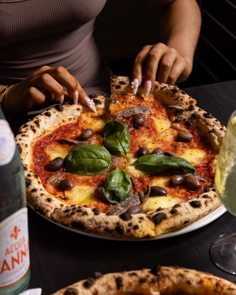 Person eating delicious wood-fired pizza with basil.