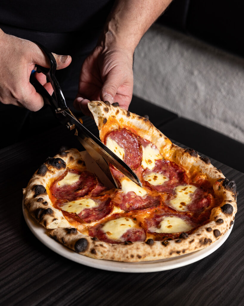 Person cutting pepperoni pizza with scissors.