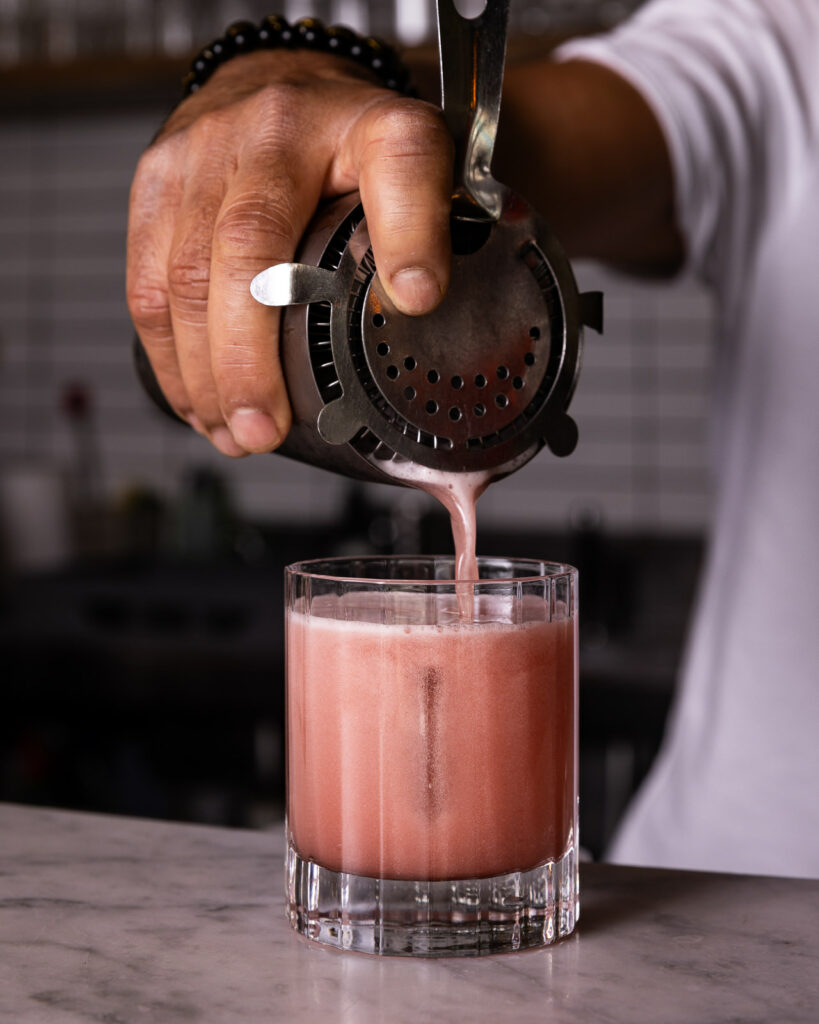 Bartender straining mixed drink into glass on counter.