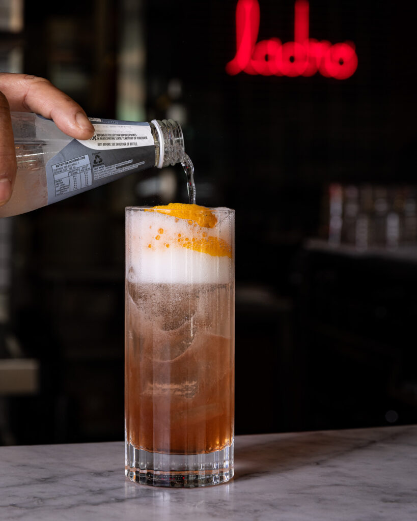 Pouring tonic into cocktail with orange garnish