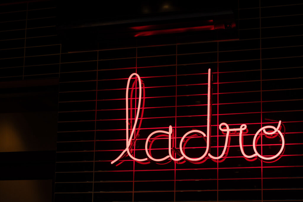 A red neon sign on a wall covered in black tiles.