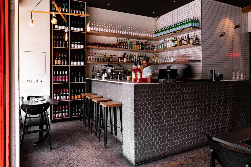 Cozy bar interior with shelves of bottles, stools.