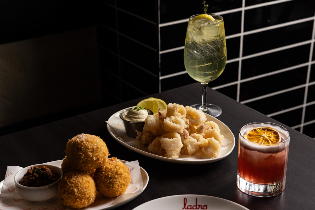 Calamari, arancini, and cocktails on a dark table.