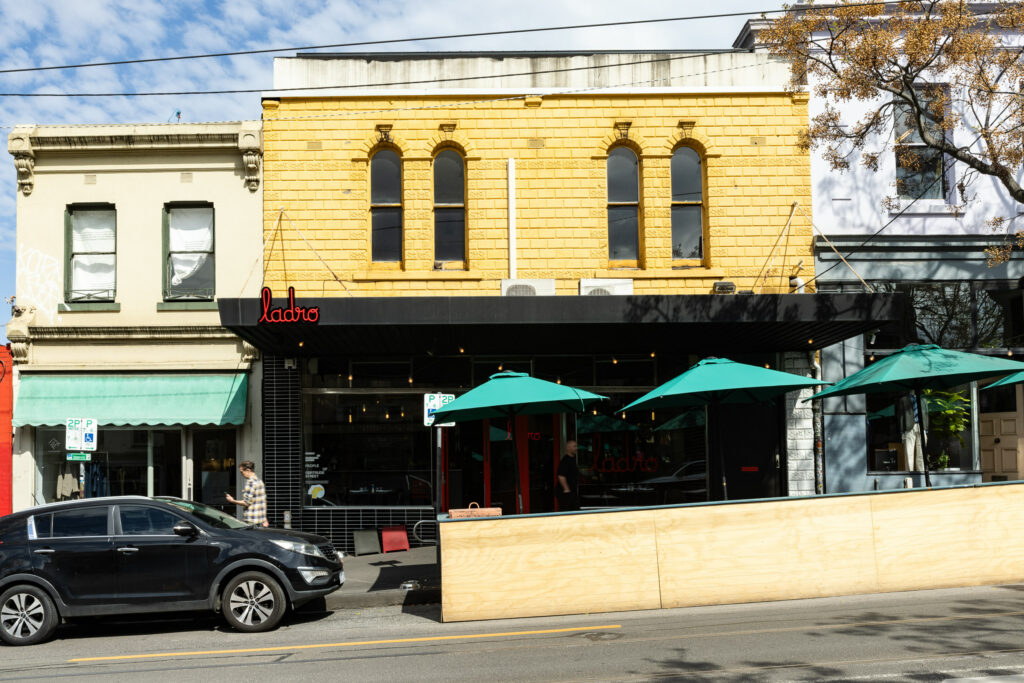 Street view of restaurant with umbrellas and car.