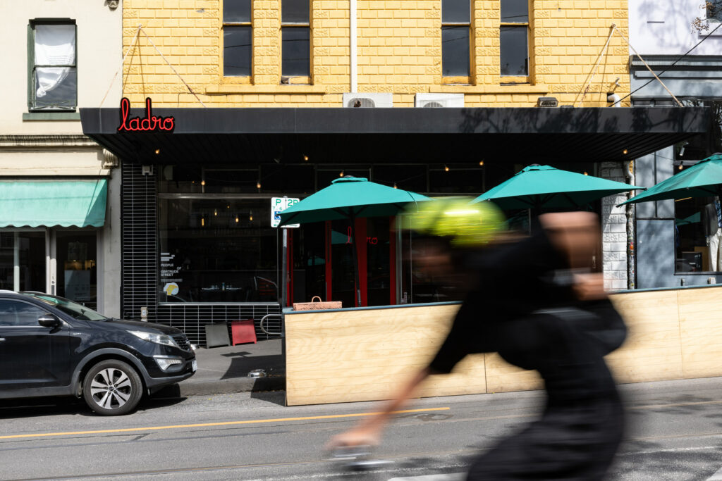 Cyclist passing by a restaurant with green umbrellas.