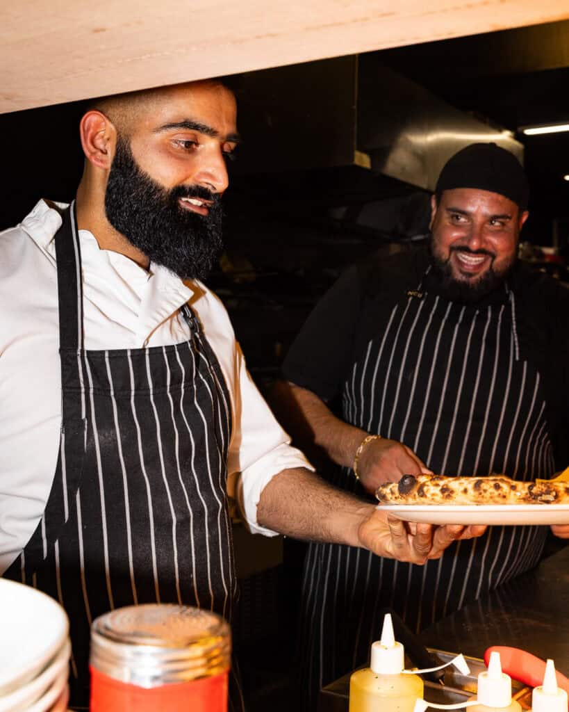 Chefs in kitchen serving freshly made pizza.