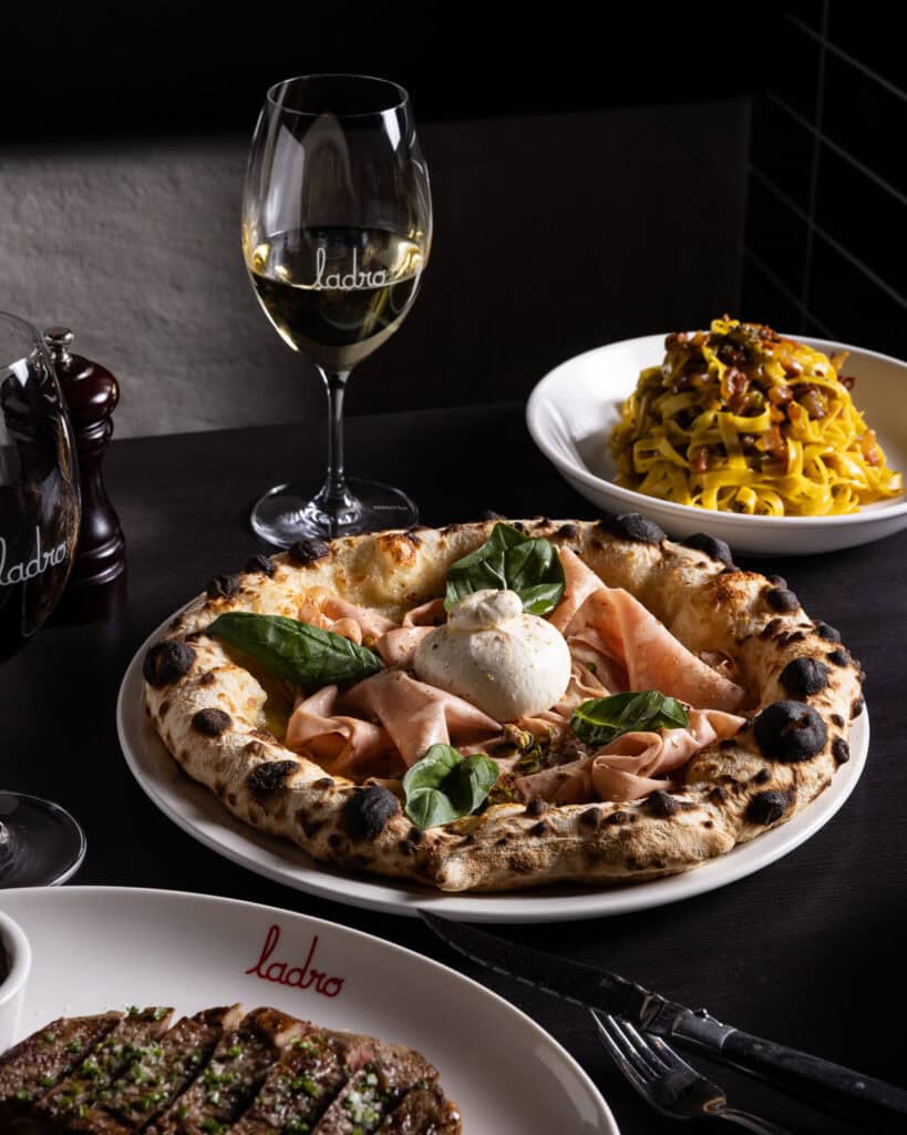 Gourmet pizza, pasta, steak, and wine on table.
