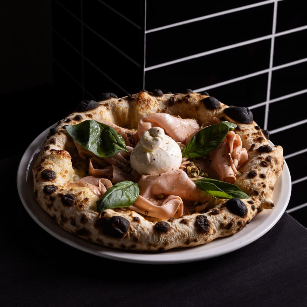 Gourmet pizza with basil and burrata on plate.