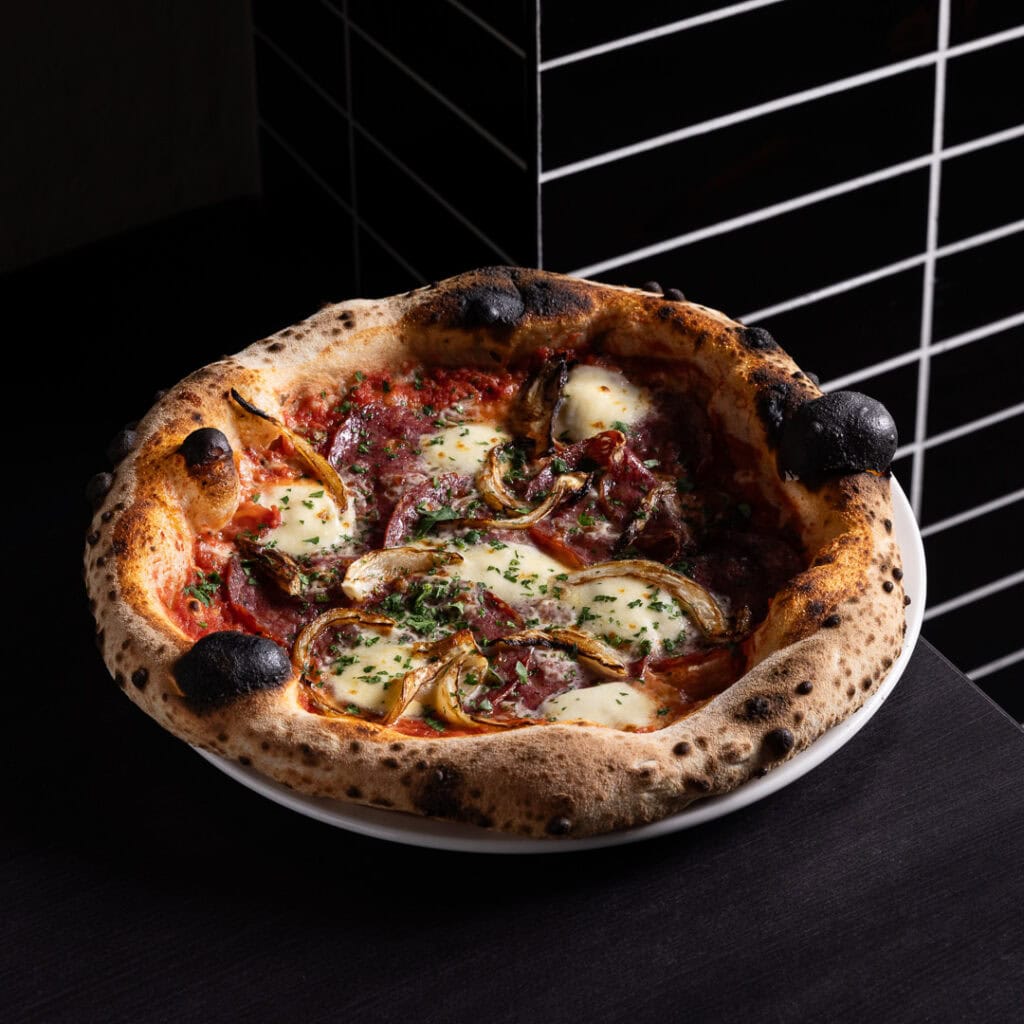 Wood-fired pizza with cheese and herbs on table.
