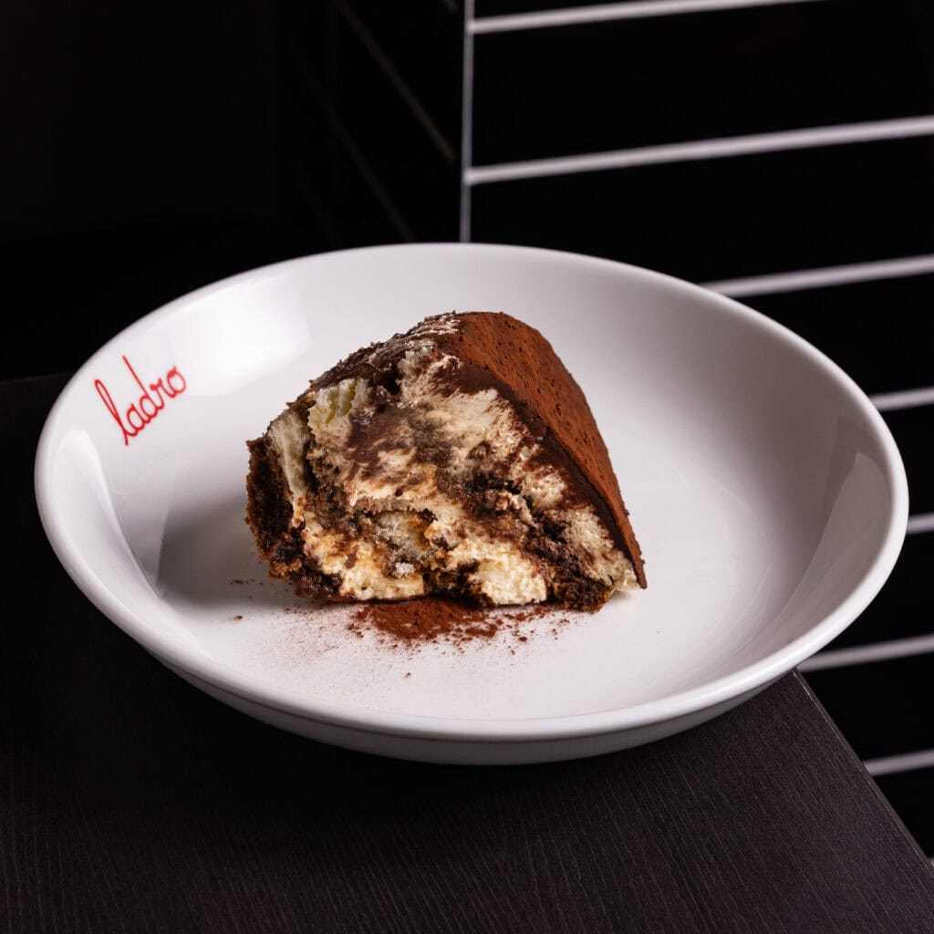 Slice of tiramisu dessert on white plate.