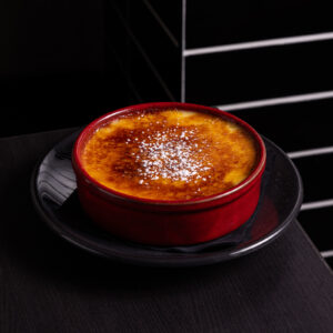 Crème brûlée with caramelized top in red dish.